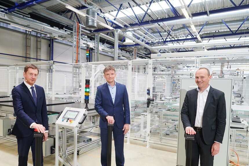 Drei Männer stehen in einer Produktionshalle und drücken auf einer Buzzer.