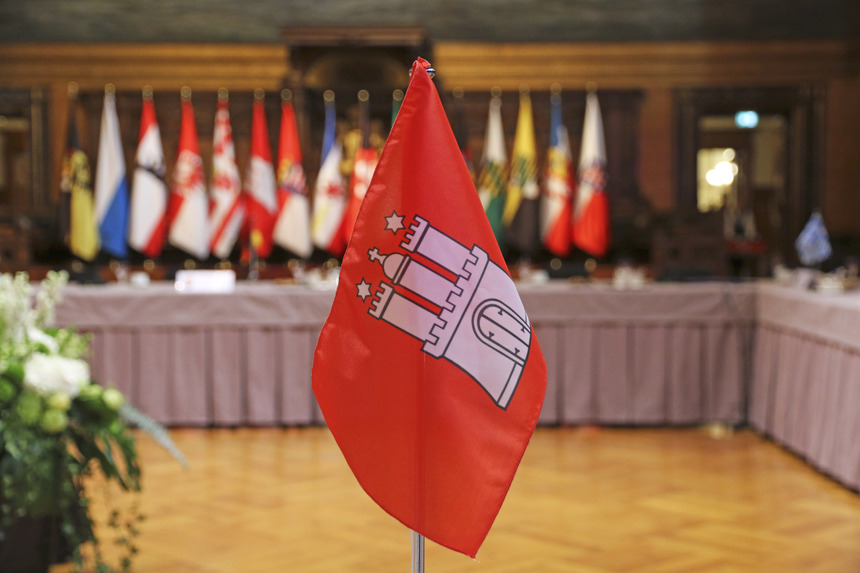 Eine Tischflagge der Stadt Hamburg. Im Hintergrund steht ein Tisch un U-Form.