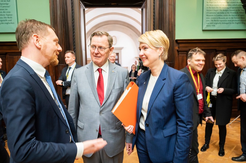 Zwei Männer und eine Frau unterhalten sich in einem großen Saal.