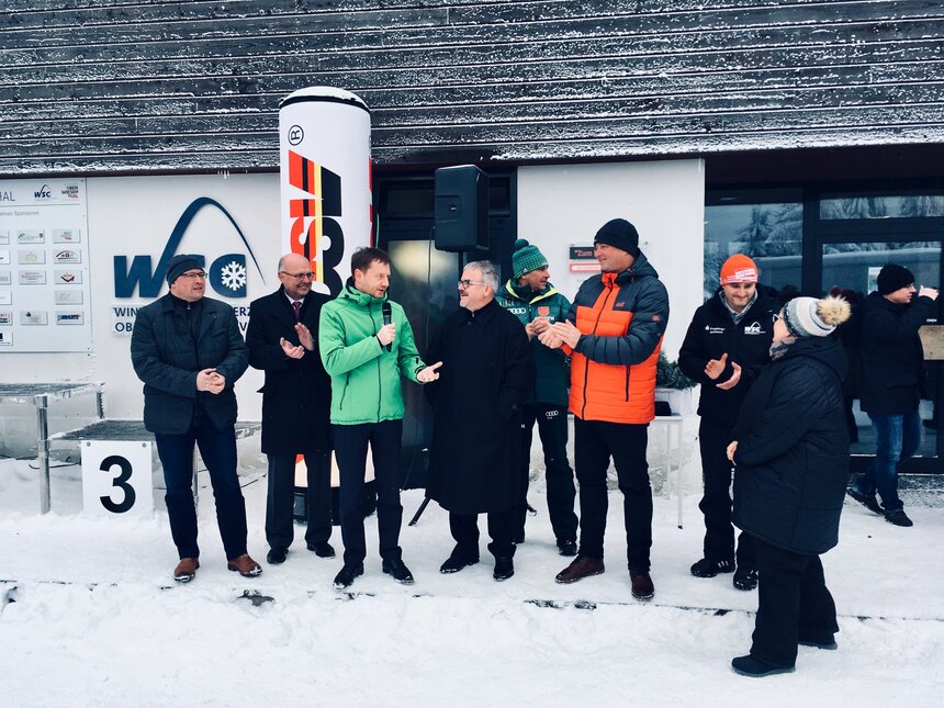 Männer und Frauen stehen in Winterkleidung vor einer Skihütte.