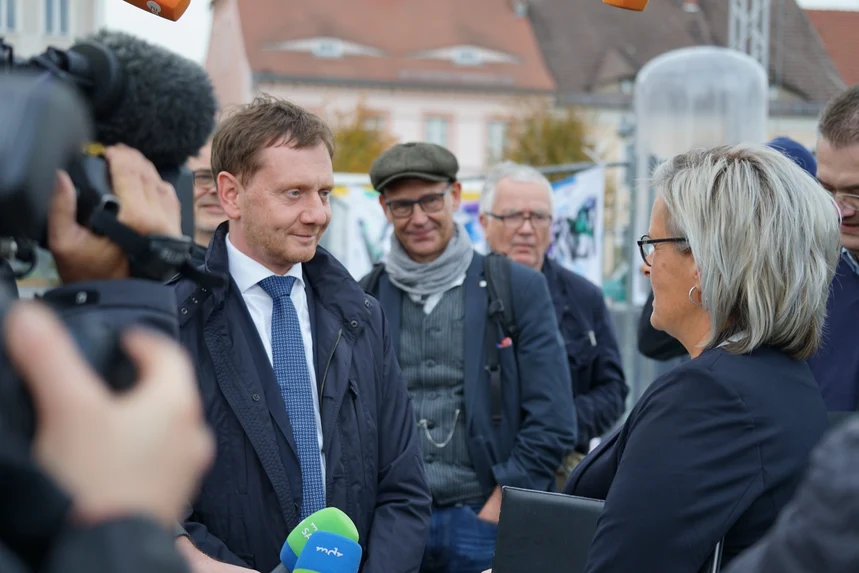 Ein Mann unterhält sich mit einer Frau. Um beide herum stehen Reporter.