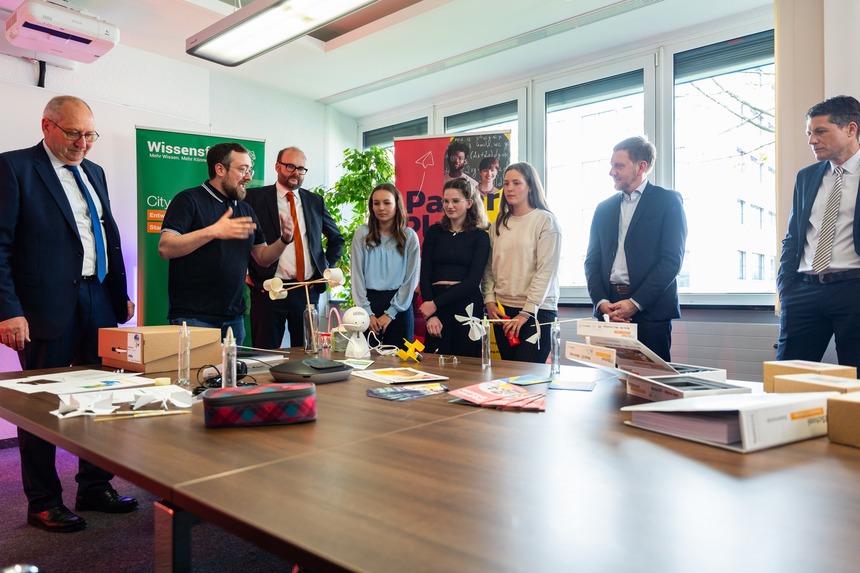 Männer und junge Frauen blicken auf einen Konferenztisch, auf dem wissenschaftliche Utensilien stehen.