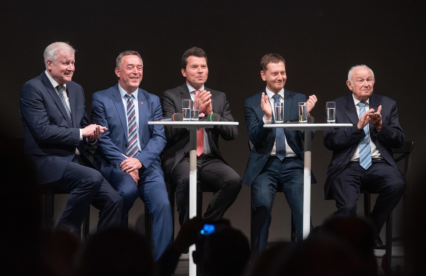 Männer sitzen in einem Podium eines Theaters.