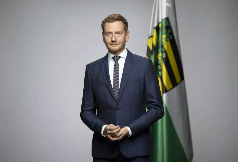 Ein Mann steht vor einer sächsischen Flagge.