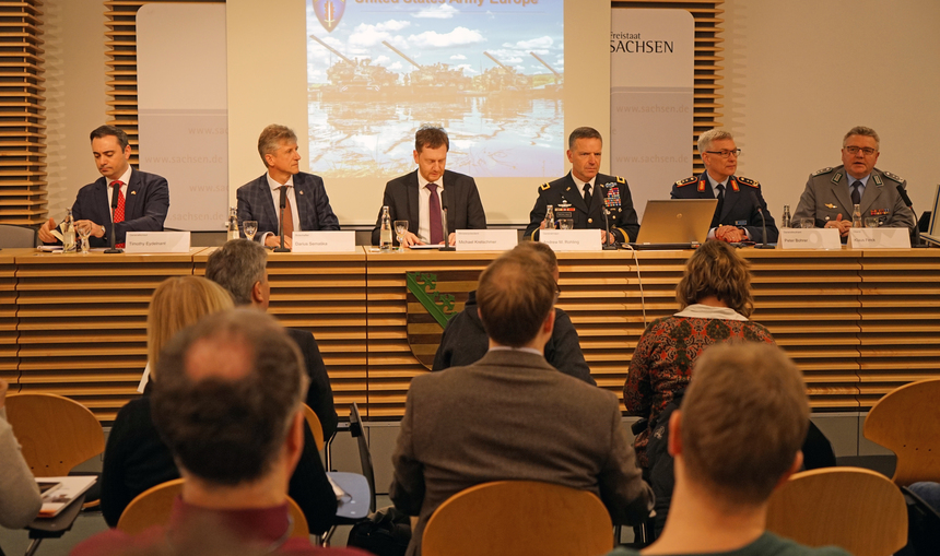 Männer sitzen auf einem Podium und halten eine Pressekonferenz.