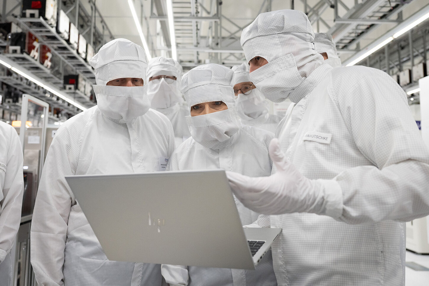 Zwei Männer und eine Frau stehen in Reinraumanzügen in einer Produktionsanlage und schauen auf einen Laptop.