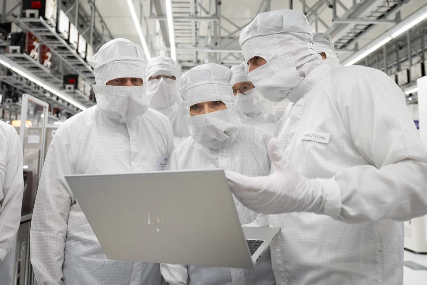 Zwei Männer und eine Frau stehen in Reinraumanzügen in einer Produktionsanlage und schauen auf einen Laptop.