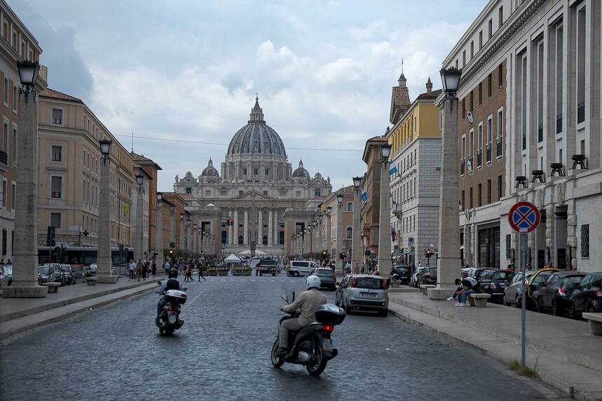 Der Petersdom in Rom. Davor eine Straße, auf der Motorroller fahren.