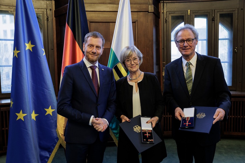 Zwei Männer und eine Frau posieren für ein Foto. Ein Mann und die Frau halten einen Orden in der Hand.