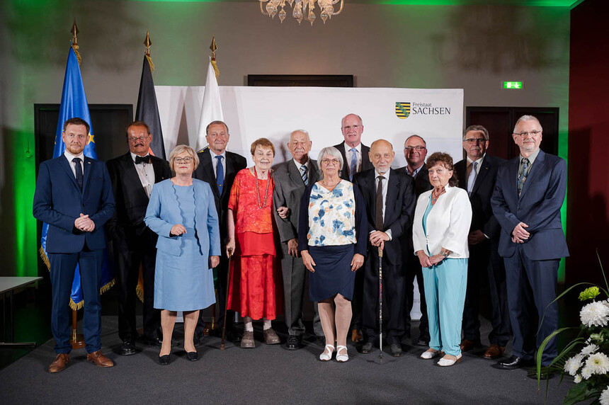 Männer und Frauen posieren für ein Gruppenfoto vor einer Fahnengalerie.