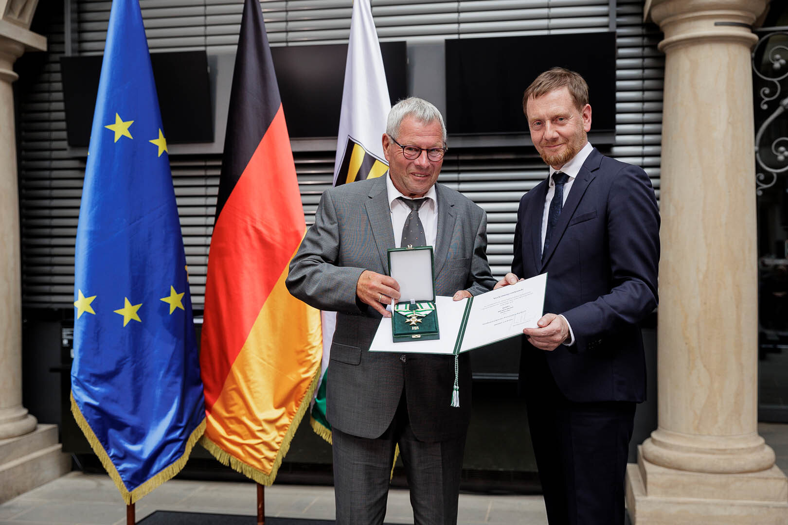 Ein Mann überreicht einem Mann einen Orden.