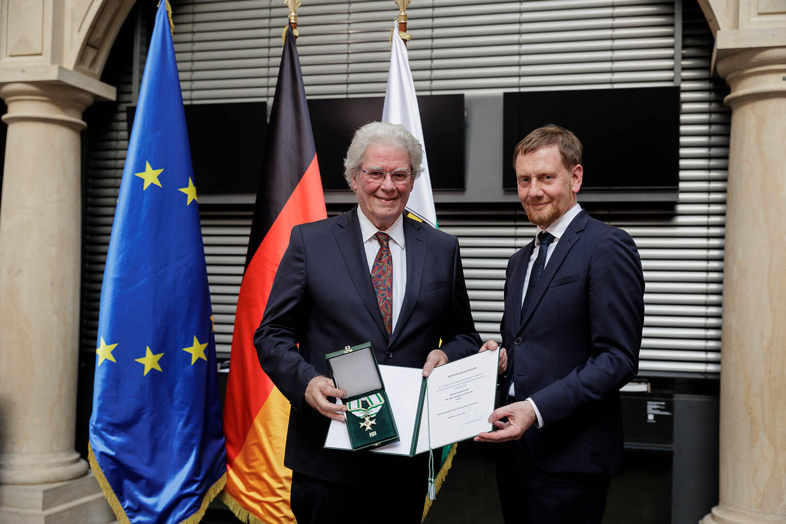 Ein Mann überreicht einem Mann einen Orden.
