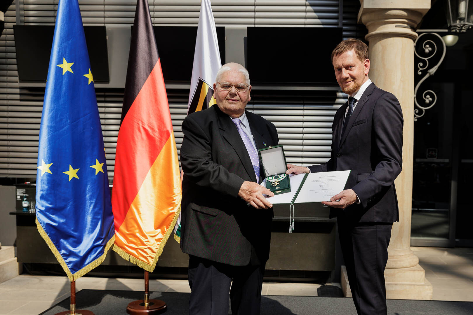 Ein Mann überreicht einem Mann einen Orden.