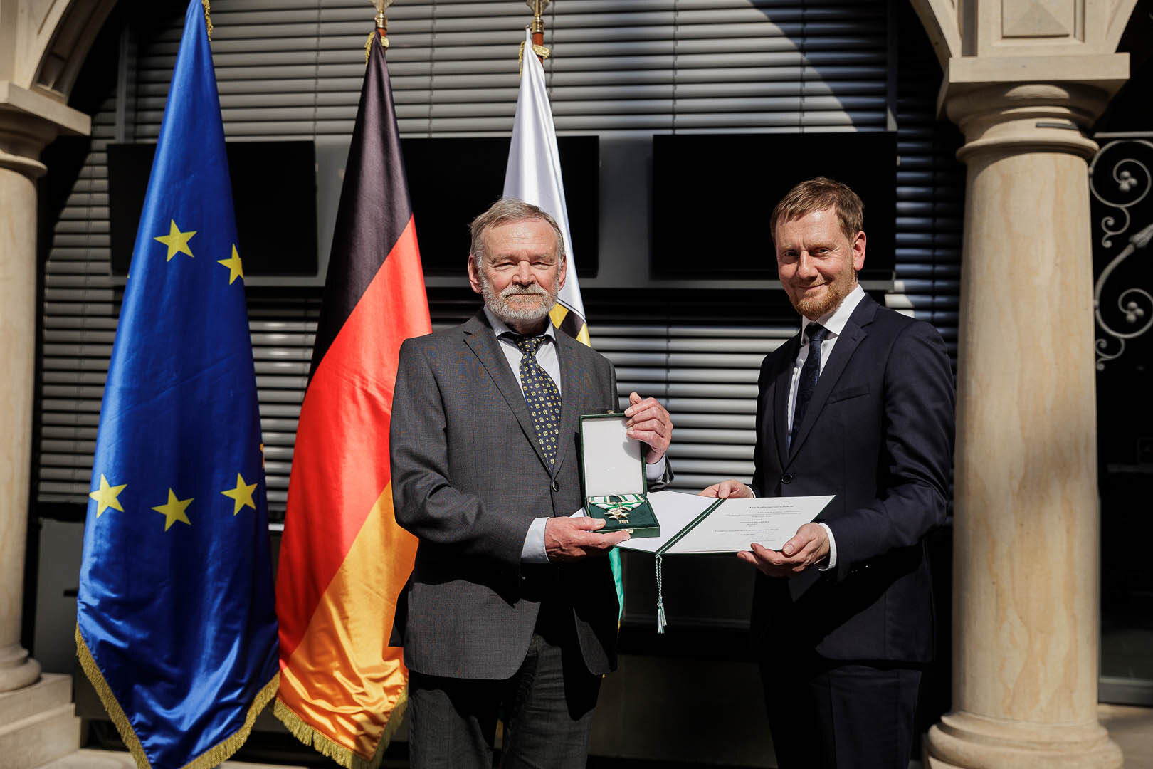 Ein Mann überreicht einem Mann einen Orden.