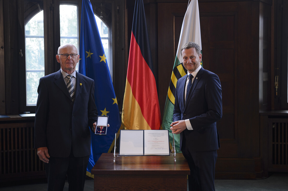 Zwei Männer stehen neben einem Pult. Einer von ihnen hält einen Ordne in der Hand.