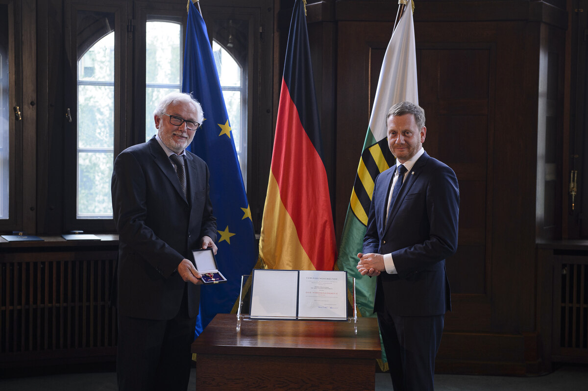 Zwei Männer stehen neben einem Pult. Einer von Ihnen hält einen Orden in der Hand.