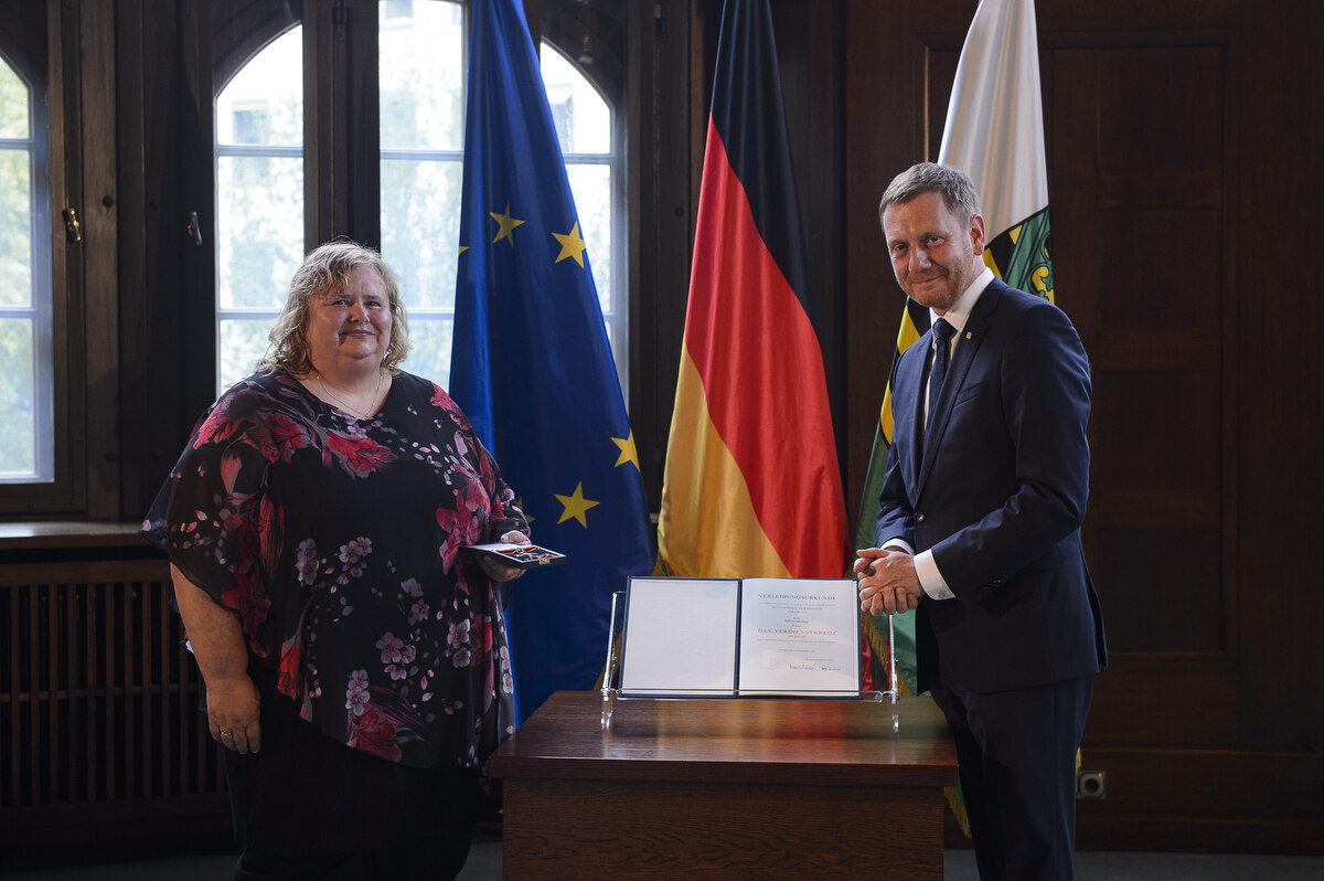 Ein Mann und eine Frau stehen an einem Pult. Eine Frau hält einen Ordne in der Hand.