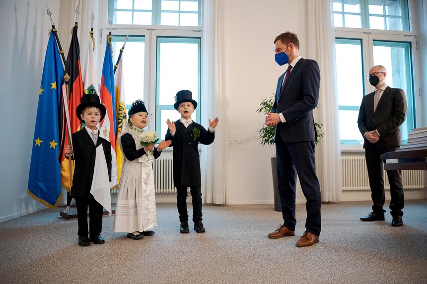 Kinder in Anzügen verkleidet stehen neben zwei Männern und singen.