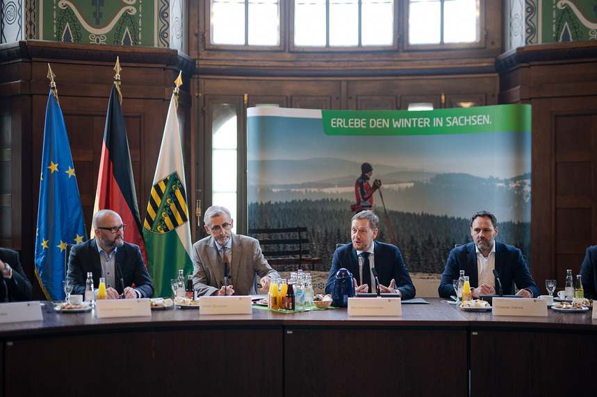 Männer sitzen vor einer Fahnengalerie an einem Konferenztisch.