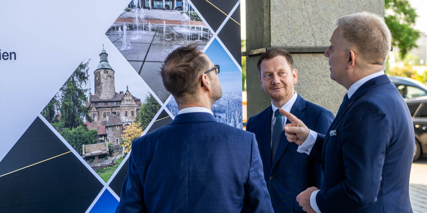 Drei Männer blicken auf eine Plakatwand.