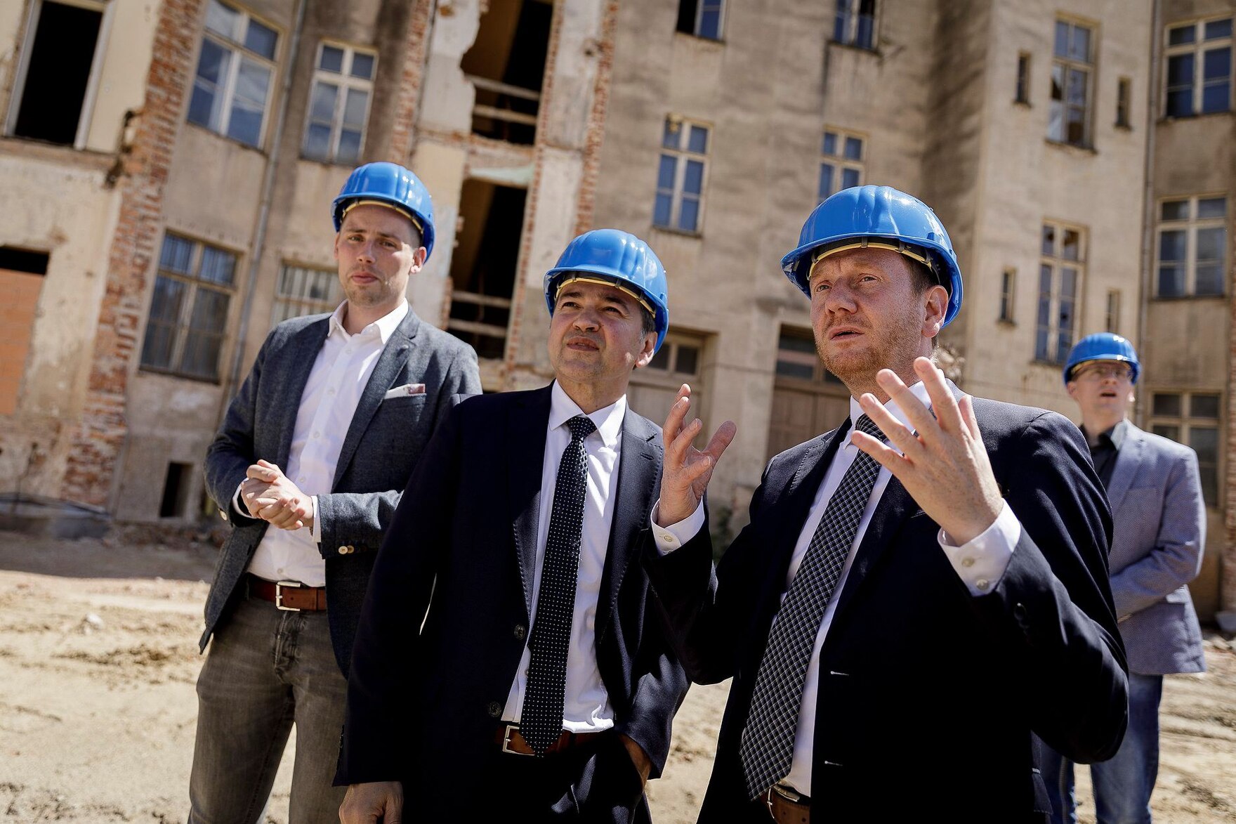 Männer mit blauen Bauhelmen auf dem Kopf besichtigen eine Baustelle.