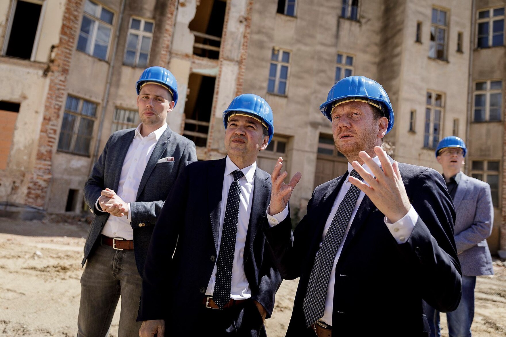 Männer mit Bauhelmen auf dem Kopf begehen eine Baustelle.