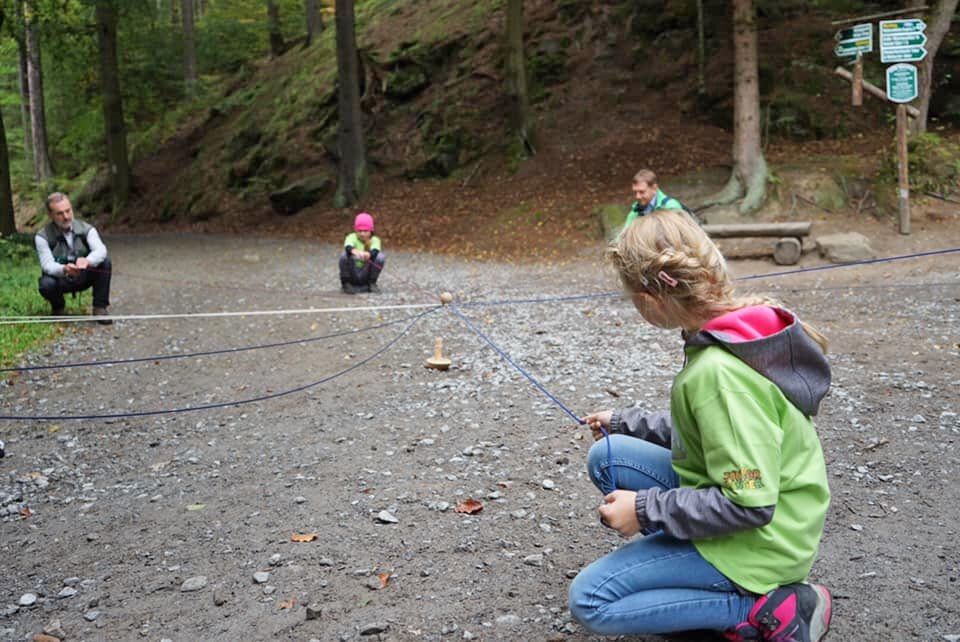 Kinder spannen ein Seil auf einem Waldboden.
