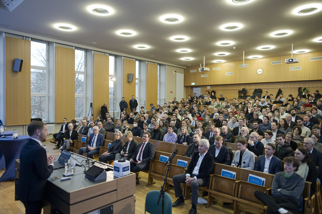 Ein Mann spricht an einem Rednerpult vor Menschen in einem Hörsaal.