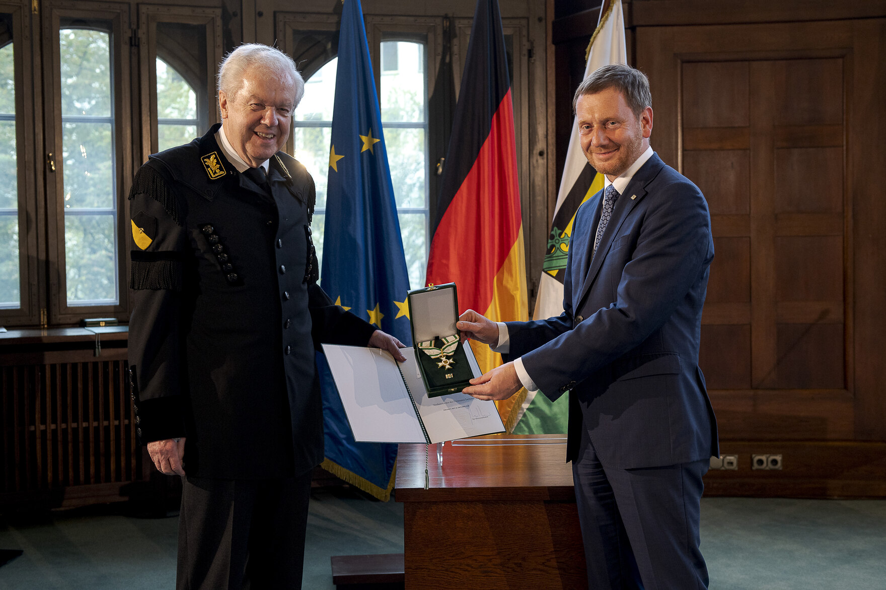 Zwei Männer stehen nebeneinander und halten einen Orden in der Hand.