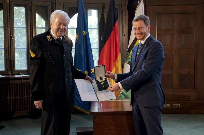 Zwei Männer stehen nebeneinander und halten einen Orden in der Hand.