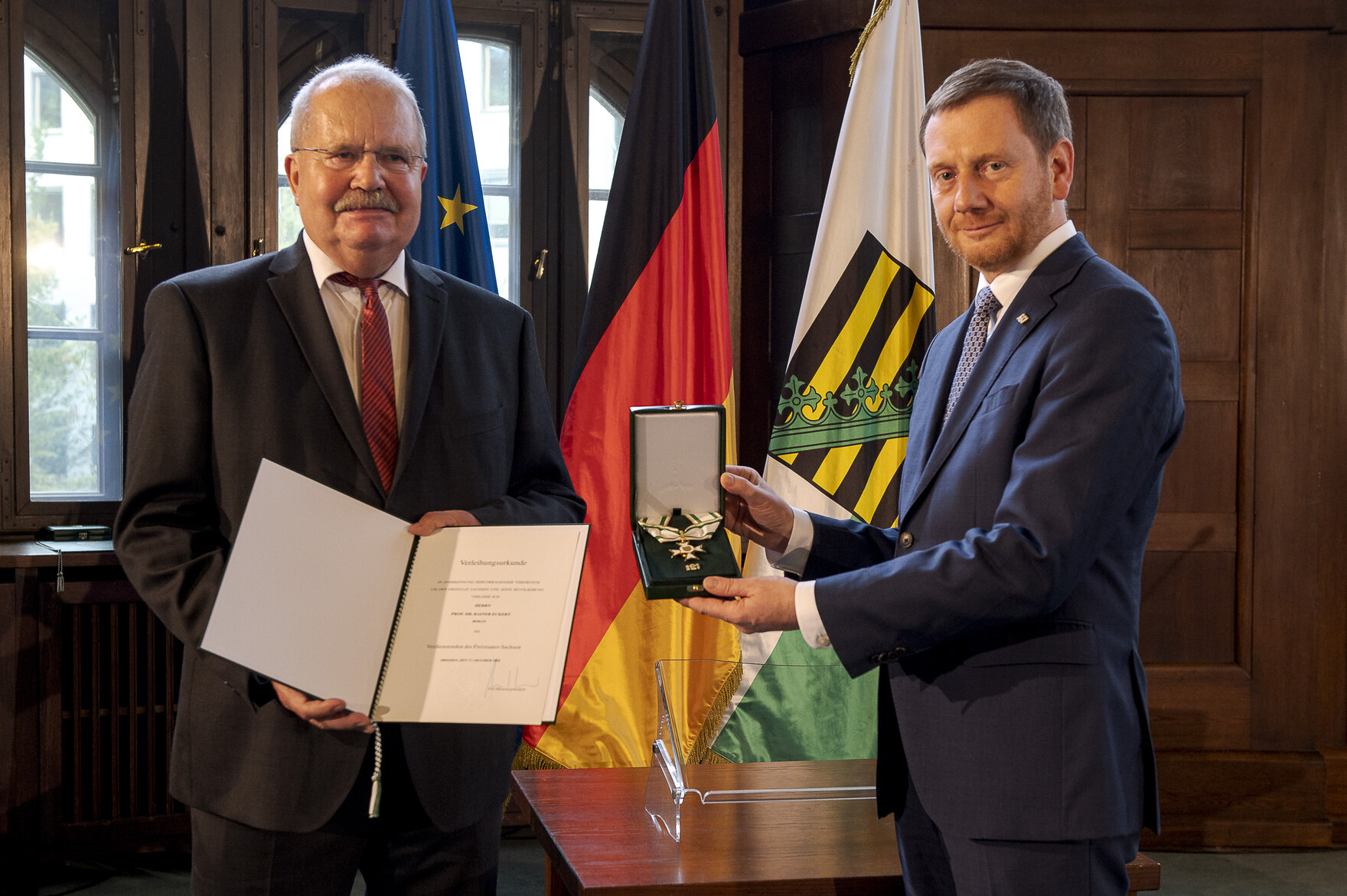 Zwei Männer stehen nebeneinander und halten einen Orden in der Hand.