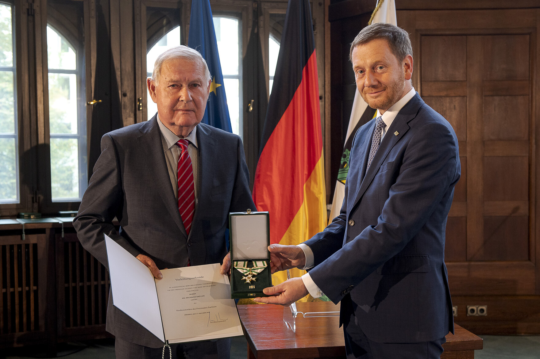 Zwei Männer halten einen Orden in der Hand.