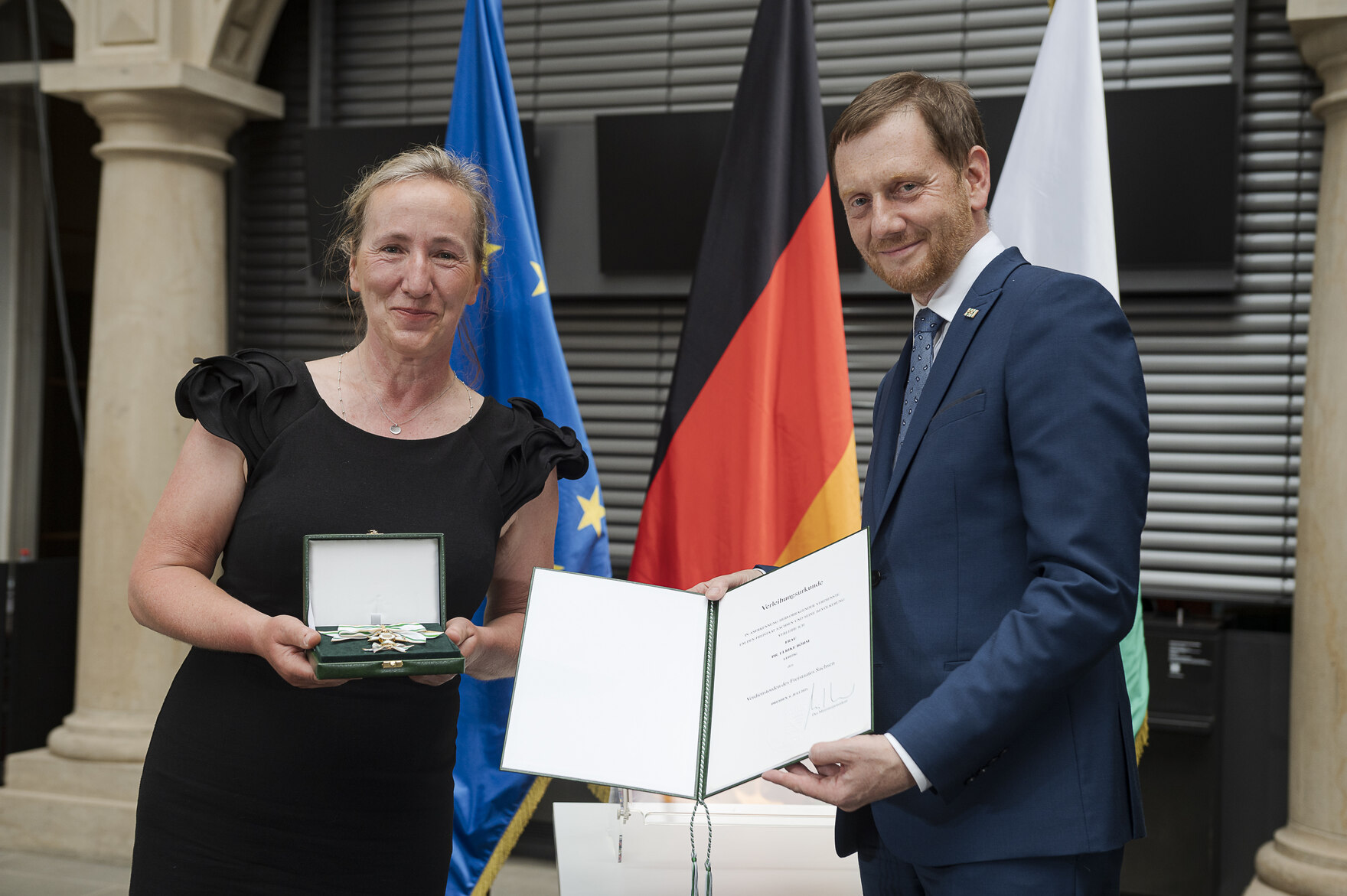 Eine Frau hält eine Urkunde in der Hand. Neben ihr steht ein Mann.