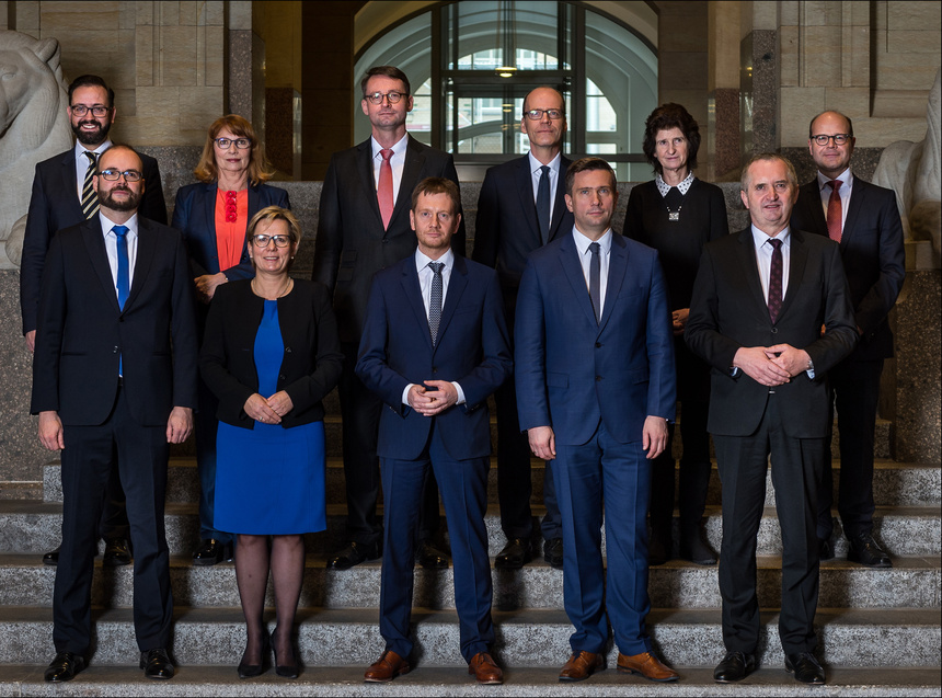 Männer und Frauen stehen in Gruppe auf einer Treppe und posieren für eine Foto.