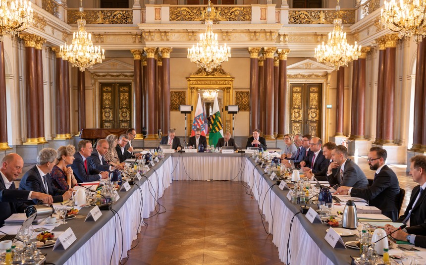 Männer und Frauen sitzen an einer Tafel.