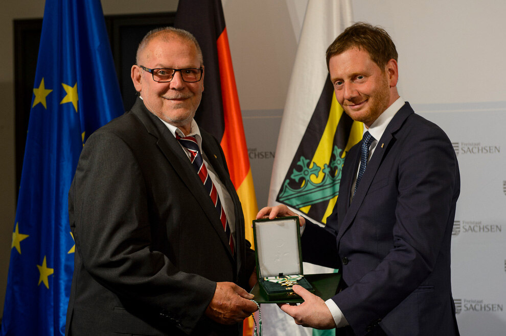 Zwei Männer halten eine Verdienstmedaille