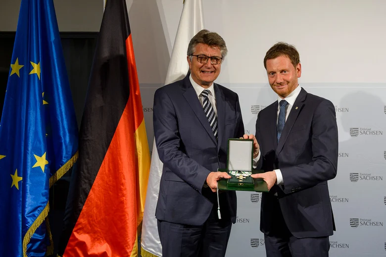 Zwei Männer halten eine Verdienstmedaille in den Händen.