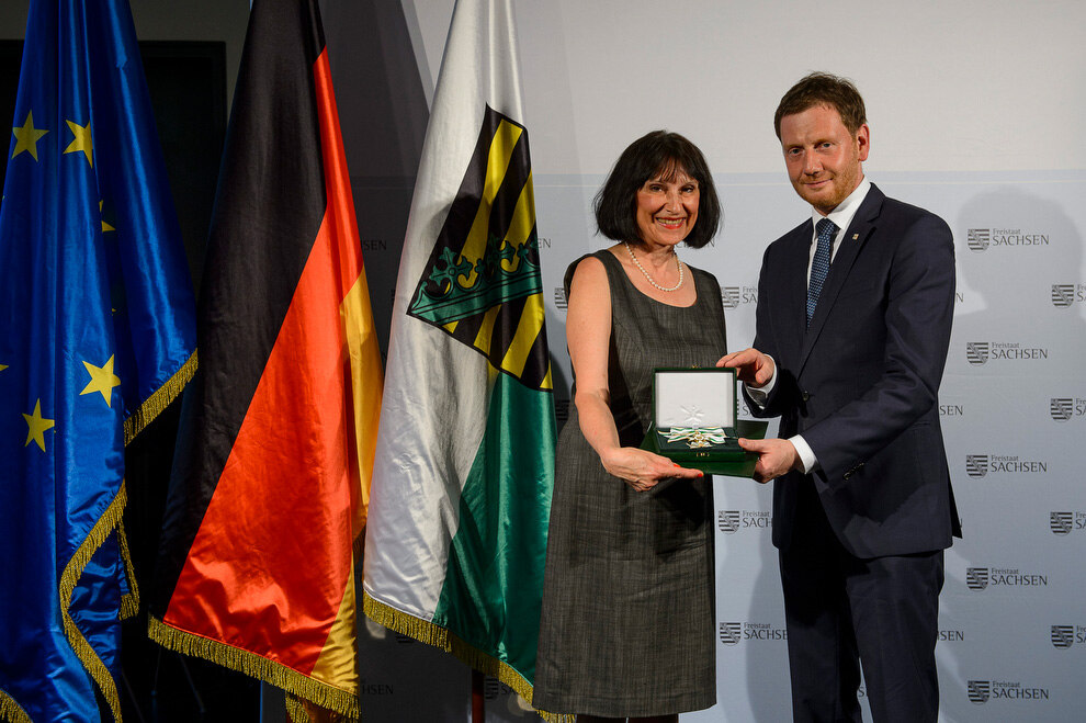 Ein Mann und eine Frau halten eine Verdienstmedaille in der Hand.