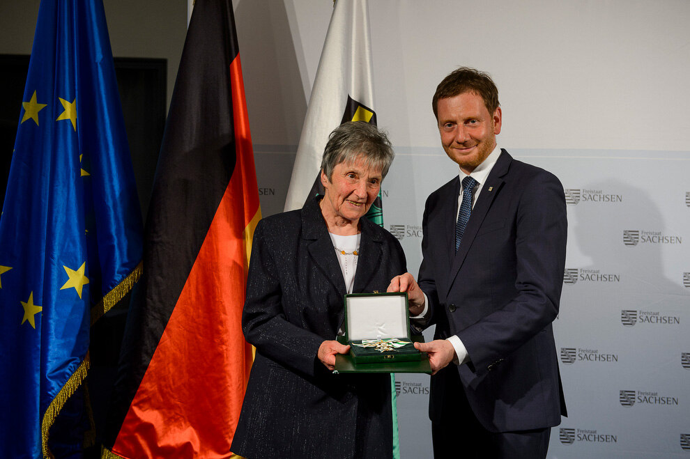 Ein Mann und eine Frau halten eine Verdienstmedaille in der Hand.