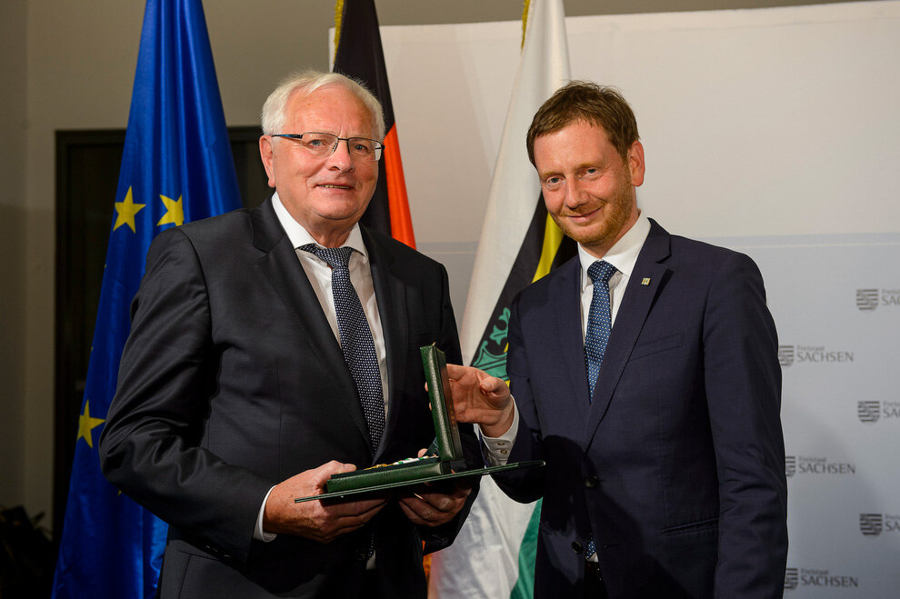 Zwei Männer halten eine Medaille in der Hand.