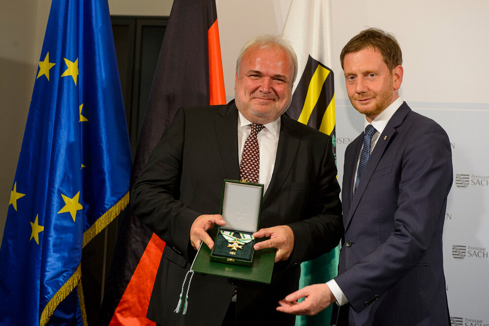 Zwei Männer halten eine Medaille in der Hand.