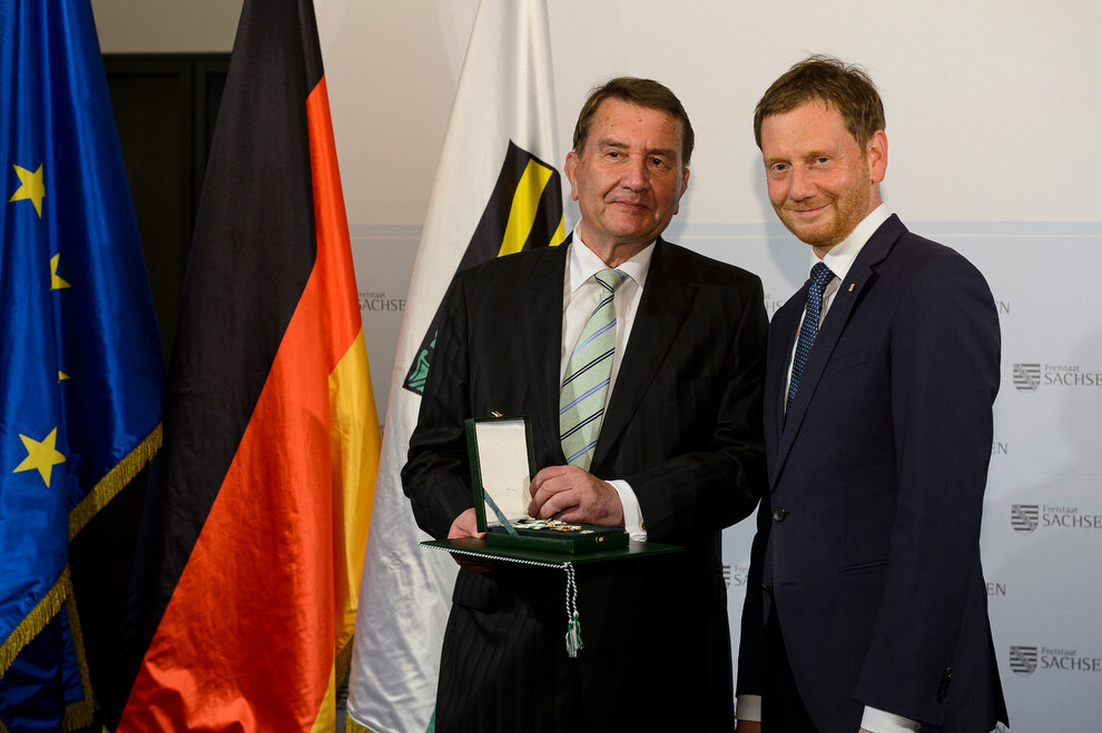 Zwei Männer halten eine Medaille in der Hand.