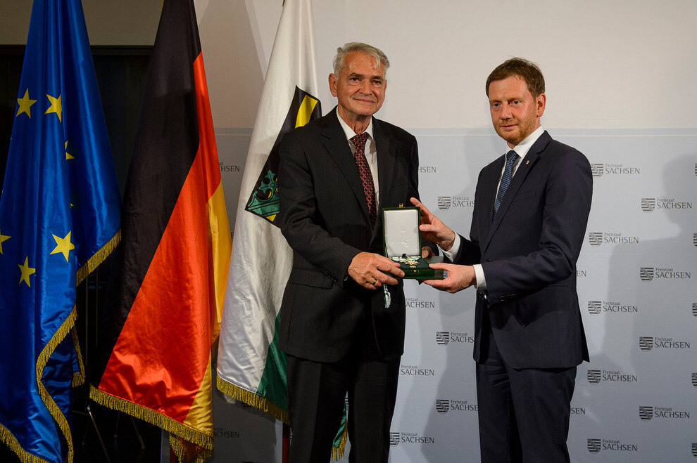 Zwei Männer halten eine Medaille in der Hand.