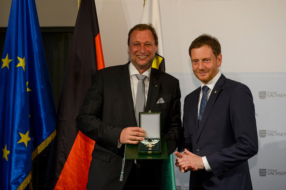 Zwei Männer halten eine Medaille in der Hand.