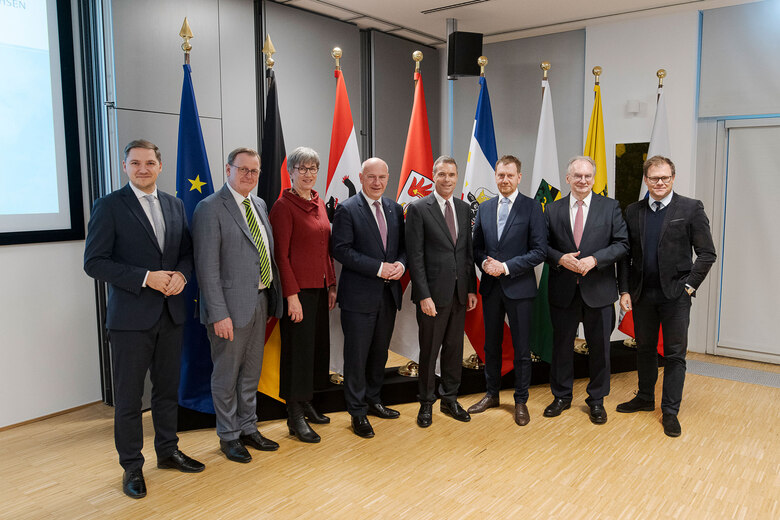 Merhere Personen posieren vor einer Fahnengalerie.